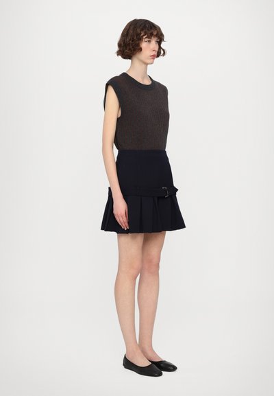 Top de punto sin mangas en gris oscuro con detalles en naranja, combinado con una falda plisada marina que presenta un detalle de hebilla lateral y zapatos negros planos.