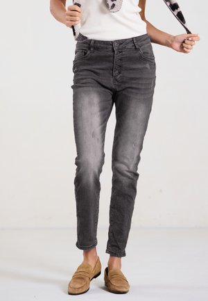Graue Skinny-Jeans aus Denim mit hoher Taille, Fünftastenverschluss und dezentem Verblassen. Kombiniert mit braunen Slippers.