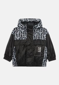 Μαύρο αδιάβροχο μπουφάν με κουκούλα, με γεωμετρικό μοτίβο και λογότυπο σε γκρι. Ελαστικές μανσέτες και μπροστινής τσέπης με καπάκι.