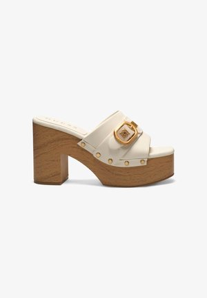 Mule bianca in pelle con tacco alto, suola platform in legno e tacco spesso, con una grande fibbia dorata e dettagli borchiati sulla cinghia.