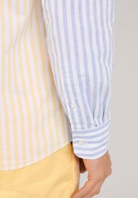 Camisa abotonada con rayas alternas azules y blancas de un lado, y rayas amarillas y blancas del otro, fabricada en un tejido ligero y con puños.