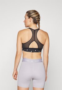 Sorte sports BH med racerback-design og nettdetaljer, med en logobånd. Kombinert med lysegrå kompresjonsshorts med logobånd.