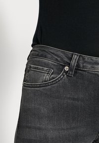 Jeans de mezclilla negra con un diseño clásico de cinco bolsillos, con una cintura de altura media, un ligero desgaste y herrajes en color plateado.