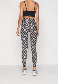Černá sportovní podprsenka s tenkými ramínky, kombinovaná s vysokými legínami s hexagonálním černobílým vzorem, doplněná sportovními botami.