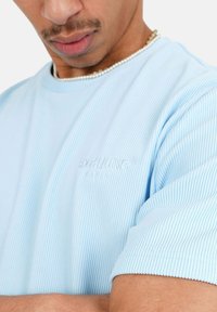 Hele sinine ribaga T-särk lühikeste varrukatega ja broderitud logoga. Sile tekstuur ja lõdva istuvusega, esitleb peeneid õmbluse detaile.