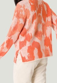 Stickad tröja med ett djärvt mönster i orange och rosa, med avslappnad passform, sänkt axel och slitsar i sidorna vid fållen.