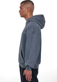 Hall griist kangast seguhoodie, millel on kangaari tasku, lahtine lõige, soonikkoes varrukad ja ääreosa. Esipoolt kaunistab brodeeritud tekst.