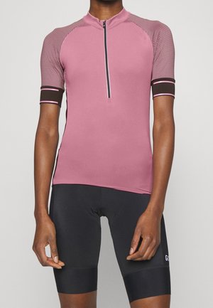 Person iført en tætsiddende lyserød cykeltrøje med sorte og lyserøde ærmer og sorte cykelshorts.