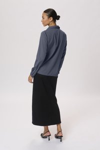 Blouse bleu marine à manches longues avec un col, associée à une jupe longue noire. L'ensemble présente une texture lisse et peu de détails métalliques.