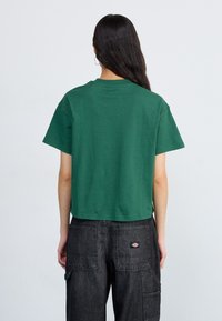 T-shirt verde a maniche corte realizzato in morbido cotone, con scollo rotondo, abbinato a pantaloni cargo scuri.