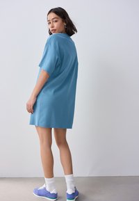 Rochie tricou supradimensionată bleu deschis din bumbac, cu mâneci scurte și croială dreaptă, asortată cu teniși mov și șosete albe.