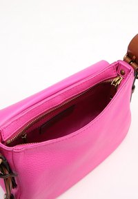 Bolso de mano de cuero rosa brillante con correa ajustable marrón, cremallera abierta que revela un interior vacío y un pequeño bolsillo interior con cremallera.