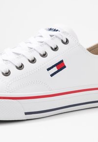 Białe skórzane sneakersy z okrągłym noskiem. Posiadają metalowe oczka, białe sznurówki, czerwone i granatowe paski na podeszwie oraz haftowane logo w kolorach czerwonym, białym i niebieskim.