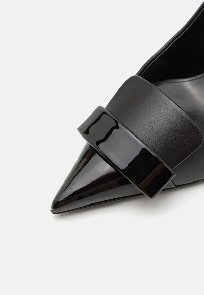 Fűzött orrú fekete cipő, amelynek lakkbőr pántja van; sima bőrfelülete és éles sziluettje elegáns megjelenést kölcsönöz.