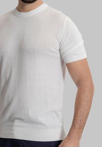 Maglietta a maniche corte bianca in maglia con colletto a girocollo. Presenta polsini e orlo a coste. Texture morbida e design aderente.