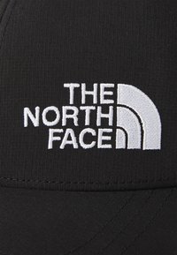 Fekete sapka, a "THE NORTH FACE" fehér logójával hímezve és ívelt formával. Simább tapintású és struktúrált formájú.