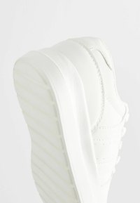Baskets blanches avec un dessus en cuir texturé, une semelle épaisse aux rainures horizontales et de subtils détails de couture le long des panneaux.