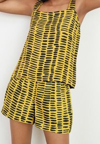 Conjunto de top sin mangas amarillo y pantalones cortos con patrones de puntos negros alargados, con un corte relajado y tirantes. Textura suave.