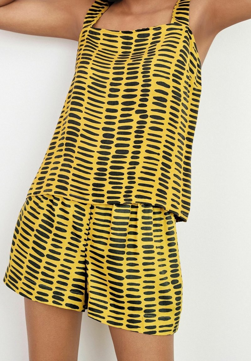 Conjunto de top sin mangas amarillo y pantalones cortos con patrones de puntos negros alargados, con un corte relajado y tirantes. Textura suave.