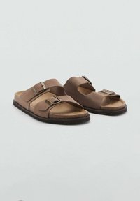 Bruine sandalen met twee verstelbare riemen, een vlakke kurken zool en metalen gespen. Het bovenmateriaal is zacht en gestructureerd.