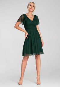 Grünes Kleid mit kurzen, transparenten Ärmeln, V-Ausschnitt, gerafftem Oberteil und ausgestelltem Rock. Glattes Material mit weicher Textur und fließendem Schnitt.