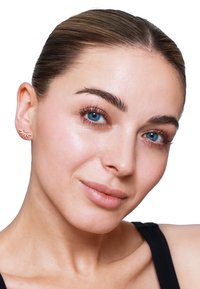Orecchini in tono oro con design a foglia, impreziositi da dettagli in cristallo trasparente. Indossati da un modella con pelle liscia e un'espressione neutra.