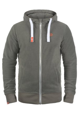 Hanorac cu fermoar din fleece gri, cu șnururi albe, buzunare frontale și un accent de logo portocalie. Are manșete și tiv din material ribbed. Textură moale.