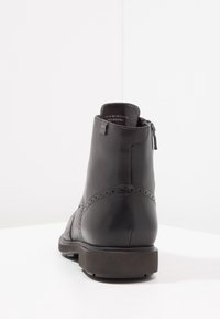 Botín de cuero negro hasta el tobillo con un acabado suave, detalles perforados y una cremallera lateral. Suela de goma sólida y un tacón bajo.