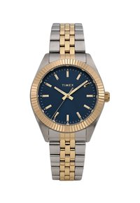 Timex-klokke med blå skive, gullfargede time markører, og en sølv- og gullfarget rustfri stålarmbånd. Har en teksturert bezel og krone.