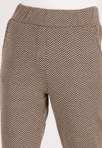 Bruine en crèmekleurige houndstooth-gepatenteerde broeken met een brede elastische tailleband en een gladde, gestructureerde stof.