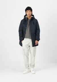 Chaqueta de puffer azul marino con capucha, camiseta gris, pantalones cargo ligeros y zapatillas blancas. Incluye cordones ajustables y bolsillos frontales.