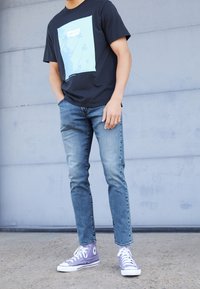 Černé tričko s modrým potiskem, světle modré džíny a fialové tenisky s vysokým svrškem. Ležérní oblečení s čistými liniemi a kontrastními barvami.