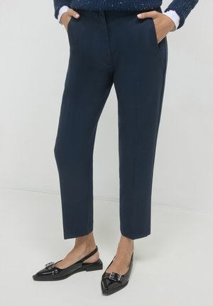 Navy-Hosen mit maßgeschneidertem Schnitt, ausgestattet mit Seitentaschen und einer glatten Textur. Kombiniert mit glänzenden schwarzen Slingback-Schuhen mit Verzierungen.