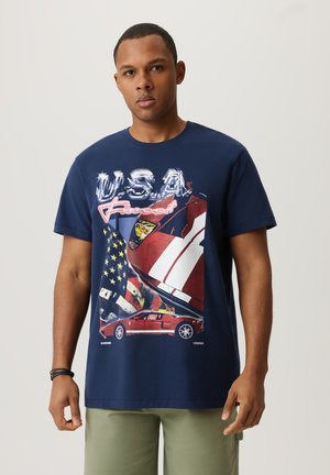 Granatowa koszulka bawełniana z graficznym nadrukiem, zawierająca elementy w kolorach czerwonym, białym i niebieskim, w tym sportowy samochód oraz akcenty z amerykańską flagą.