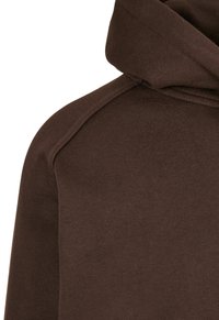 Sudadera con capucha marrón, textura suave, detalles acanalados en el dobladillo y los puños, con un ajuste holgado y costuras de hombro en ángulo.
