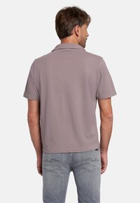 Korte mouwen, licht mauve poloshirt met een relaxte pasvorm; de achterkant toont een platte kraag en een gladde textuur in een zachte stof. Gecombineerd met lichtblauwe jeans.