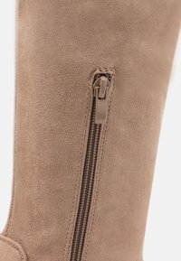 Beige mocka ankelboots med dragkedja på sidan och en brun dragflik. Boots har en slät yta och en enkel design utan ytterligare dekorationer.