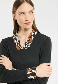 Czarna bluzka z dekoltem w serek i wzorzystym kołnierzykiem w odcieniach ziemi, uzupełniona wzorzystymi mankietami. Gładki materiał o miękkiej fakturze.