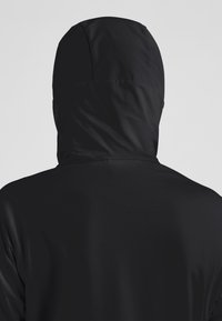 Giacca nera con cappuccio realizzata in un materiale liscio e leggero. Caratterizzata da un cappuccio aderente e un design minimalista senza dettagli hardware visibili.