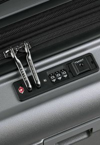 Dettaglio di una valigia rigida grigia che presenta doppi zip, una serratura TSA con combinazione a manopola e una superficie strutturata per una migliore presa.