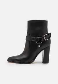 Czarny skórzany botek za kostkę z szpiczastym noskiem, srebrnym elementem ozdobnym w formie klamry, regulowanym paskiem oraz słupkowym obcasem. Gładka faktura z minimalną ilością detali.