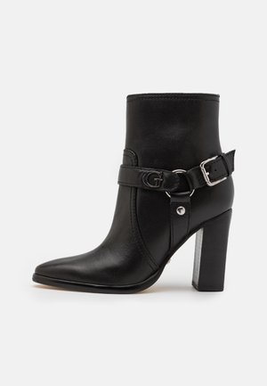Bota de cuero negra hasta el tobillo con punta afilada, hebilla plateada, correa ajustable y tacón bloque. Textura lisa con detalles mínimos.