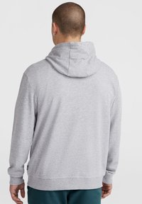 Un sweat à capuche gris fait d'un matériau doux, avec un cordon de serrage, des manches longues et des poignets côtelés. Détails de couture visibles.