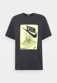 Svart bomullströja med en stor gul grafik med en Nike-logotyp och abstrakt design. Korta ärmar och rund halsringning.