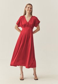 Robe midi en satin rouge avec manches courtes volantées, décolleté en V et corsage ajusté s'évasant en une jupe fluide. Présente une texture lisse et brillante.