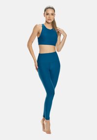 Sujetador deportivo en color teal y leggings de cintura alta hechos de material elástico. Diseño sin costuras con una textura suave y detalles de costura mínimos.