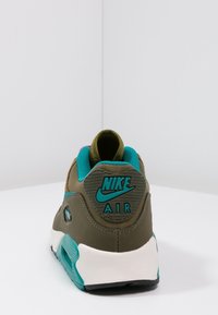 Nike Air tenisky s horní částí v zelené a tyrkysové barvě, polstrovaným límcem a texturovanou černou podrážkou; na patě je vyvýšené logo.