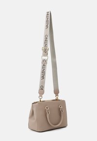 Beige läderhandväska med guldfärgade detaljer, dubbla handtag upptill och ett avtagbart bärband med en logotyp. Rektangulär form, slät textur.