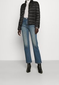 Czarna kurtka puchowa z poziomymi szwami, wysokim kołnierzem i oznaczeniem marki. Połączona z przetartymi, niebieskimi spodniami dzwonami i czarnymi botkami za kostkę.