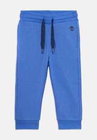 Pantaloni della tuta blu realizzati in tessuto morbido, con un elastico a coste in vita, stringhe regolabili e polsini. Include un piccolo logo decorativo.